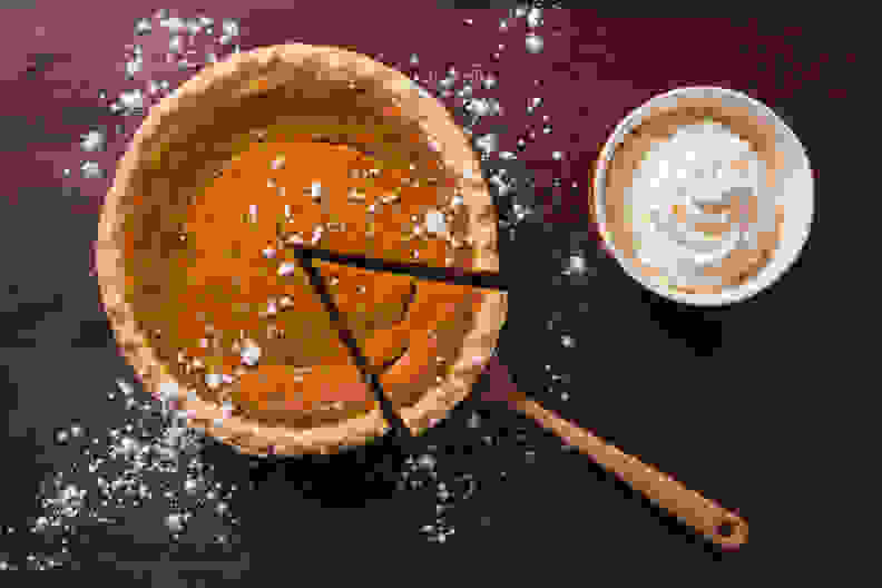 An overhead view of a gourmet pumpkin pie with a side of whipped cream on a rustic wood table surface