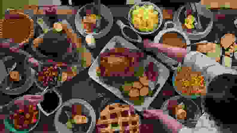 An aerial shot of a Thanksgiving table filled with food, with hands filling their plates.