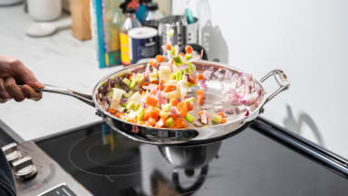 Vegetables are tossed in a stainless-steel skillet.