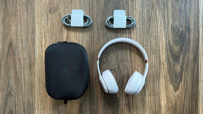 The Beats Solo 4 headphones, their case, and two cables displayed on a wooden floor.