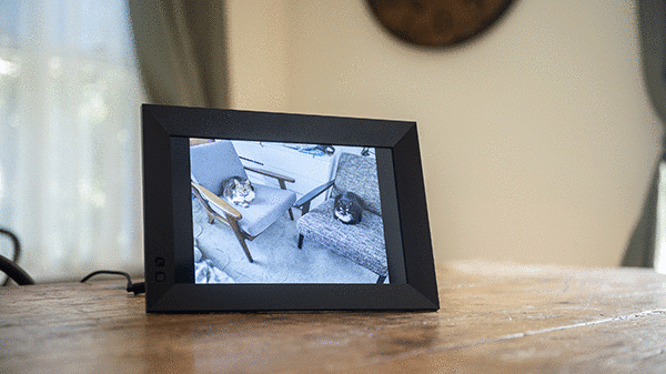 A digital picture frame displays a slideshow of images while sitting on a wooden table.