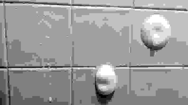An image of the tilled side of a shower, showcasing three tiles in particular, all of which have been sprayed with a cleaner. The leftmost spray is very thin and runny, with barely any foaming action visible. The middle spray is a small dollop of foam, but in the time it took us to quickly spray and take the photo it had already run down about three inches, onto the next tile. The final spray is another circular mound of foam, only this time it's stuck to the center of the tile where we initially sprayed it.