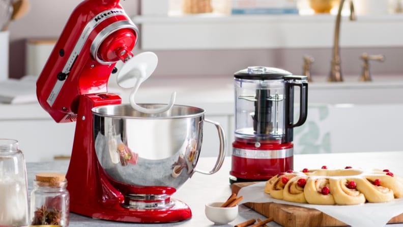 A red KitchenAid stand mixer with dough hook next to a red KitchenAid food processor on a kitchen island.