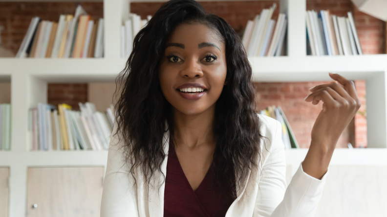 A lovely young person looks into the camera, speaking to us. Behind them, out of focus, are shelves full of print books.