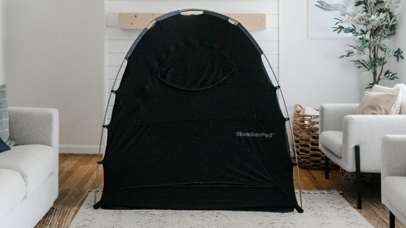 A black tent-like SlumberPod sits in the middle of a living room.