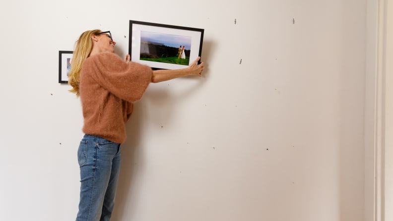 A woman hangs a photo on a wall