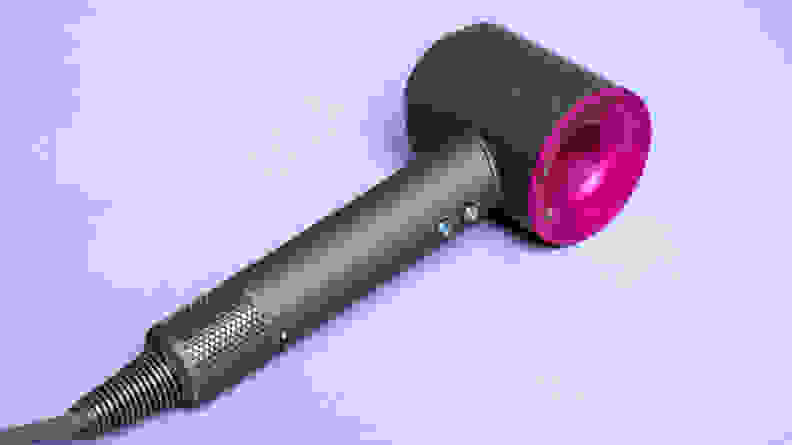 A charcoal gray and fuschia hair dryer laying on a light purple background.