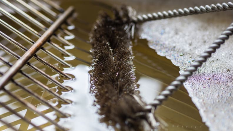 A close-up of a grill grate sitting in cleaning liquid as a brush scrubs it.