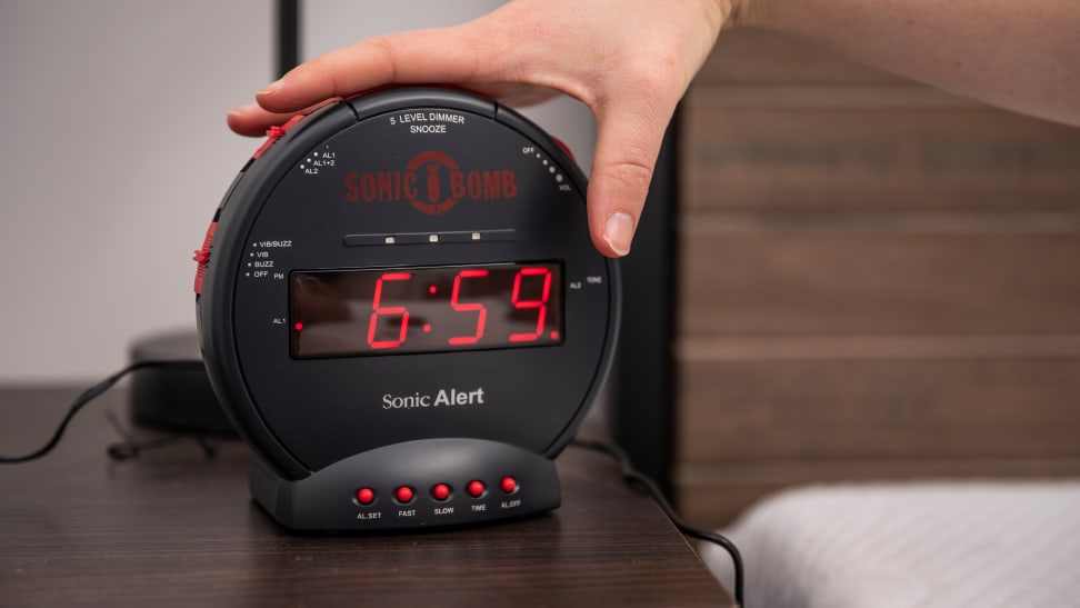 a person's hand presses the snooze button on the sonic bomb alarm