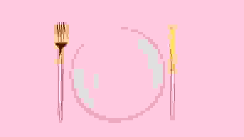 A light pink dinner plate flanked by a pink and gold fork and knife.