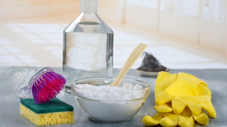 Sponge, scrubbing brush, bowl of powdered cleaning, bottle of clear solution and yellow rubber gloves.