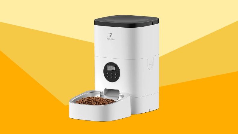 A white automatic pet feeder with food in bowl against a varied yellow background.