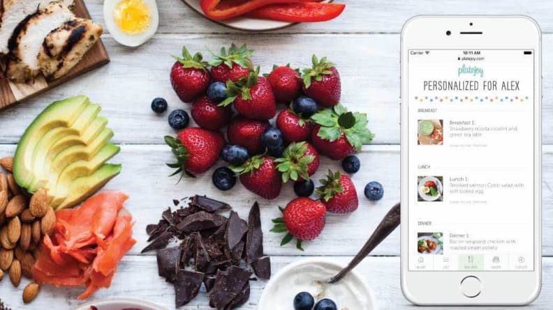 Nibs of chocolate, berries, and sliced avocado on table next to phone with PlateJoy app on it.