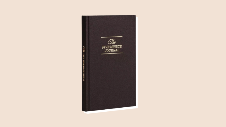 A copy of The Five Minute Journal with a black cover and gold lettering on a neutral background.