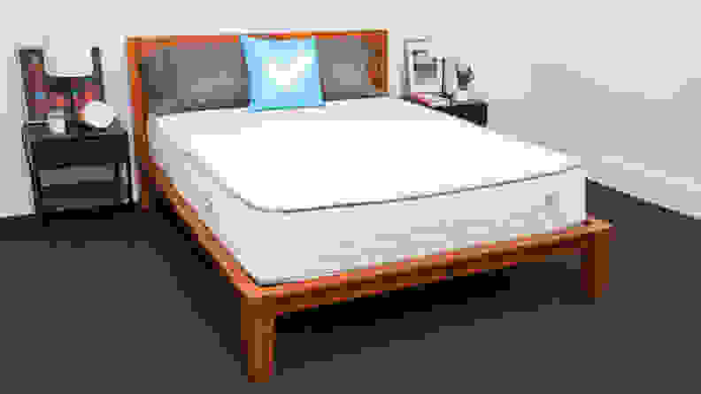 The Nolah Natural mattress inside of a wooden bed frame in a bedroom with pillows on top.