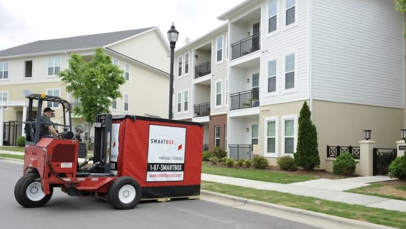 A male forklift driver delivering a small portable container box to an apartment complex