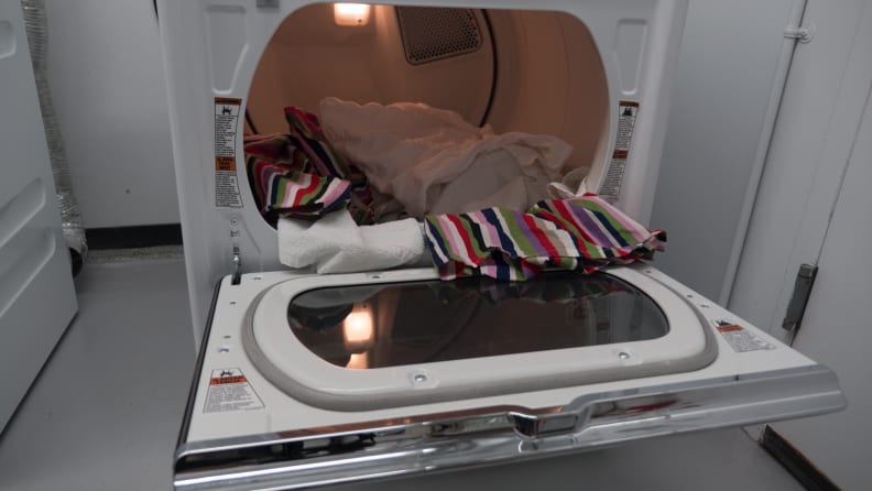 A shot of the dryer's dual-hinged door, open from top to bottom. There is a heap of laundry spilling out of the drum and onto the open door.