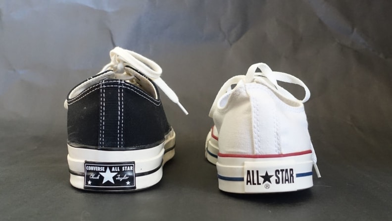 Po lewej niskie trampki Chuck 70 w kolorze czarnym.  Po prawej białe trampki z niską cholewką Chuck Taylor All Star.  Oba sneakersy mają różne logo na piętach.