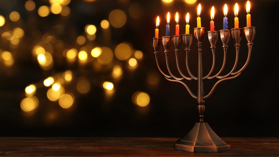 Menorah with lit, multi-color candles against a dark, candlelit background