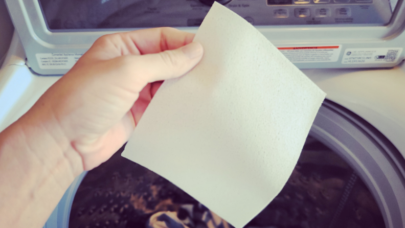 Person holding up Earth Breeze Laundry Sheets over washing machine drum.