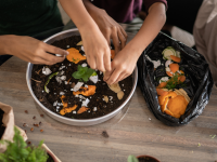 A group of people add food clippings to a compost pile.