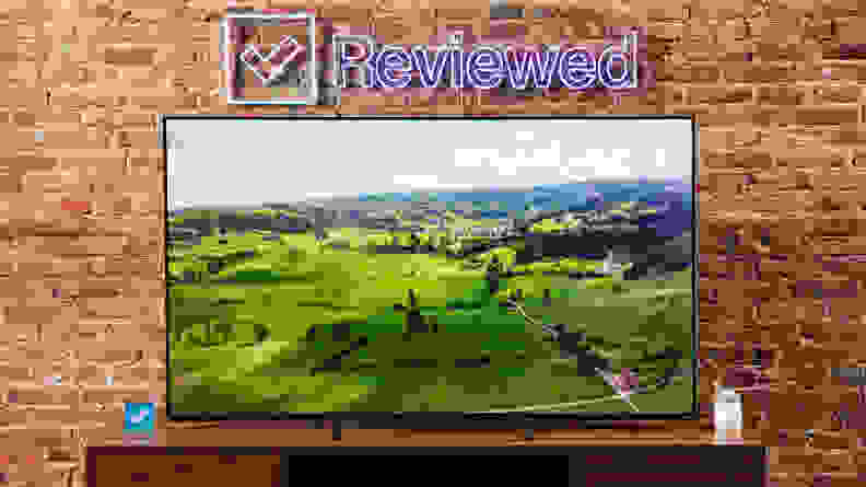 An image of the green countryside displayed on a Vizio MQX TV sitting on a wooden credenza.