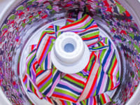 An overhead view of a top-load washer with agitator which is filled with striped sheets.