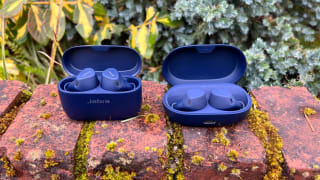Jabra's blue colored Elite 4 and Elite 7 Active earbuds sit in their open cases on a mossy brick ledge.
