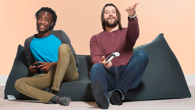 Two people play video games while sitting on a single bean bag chair like a couch.