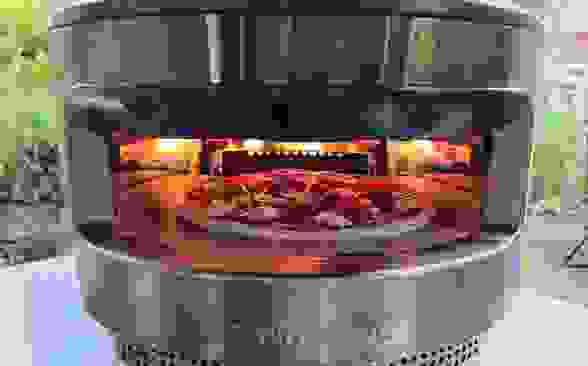 The Solo Pi sits on a counter outside. There's fire in the back of the oven and a pizza inside.