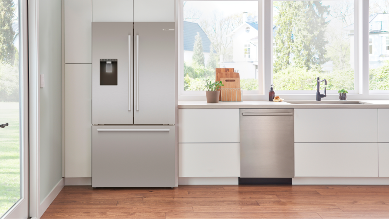 A sleek, gray Bosch refrigerator in a white kitchen with brown hardwood floors.