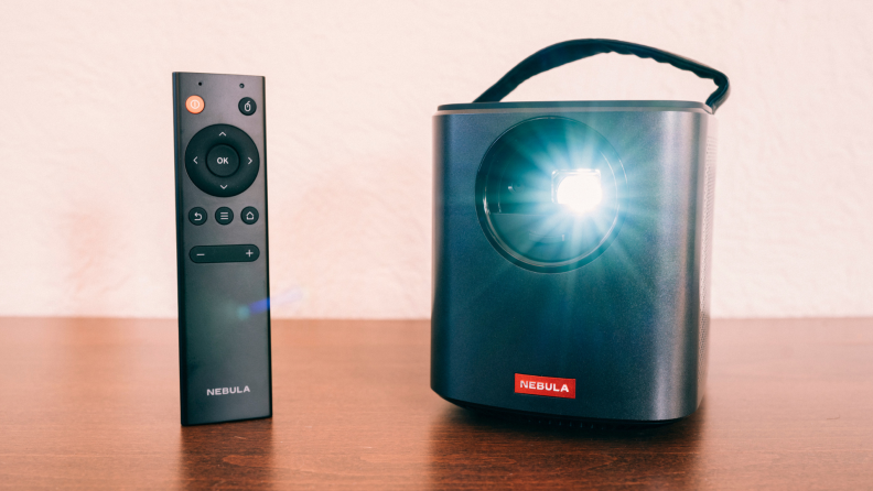 Anker Nebula Mars II portable projector and corresponding remote on a wooden surface.