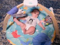 A baby laying on a Melissa & Doug Ocean Easy-Fold Play Gym on the floor.