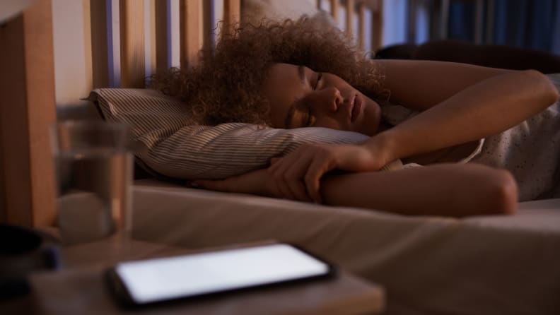 a person lies asleep next to their phone on the nightstand