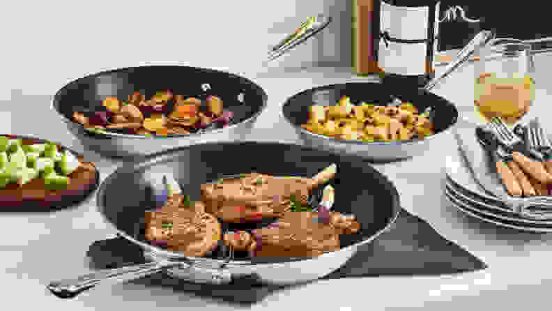 Three non-stick All-Clad frying pans of various sizes on a kitchen counter.