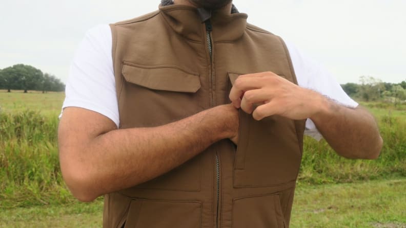 Man putting hand inside of a brown Carhartt Super Dux vest chest pocket.