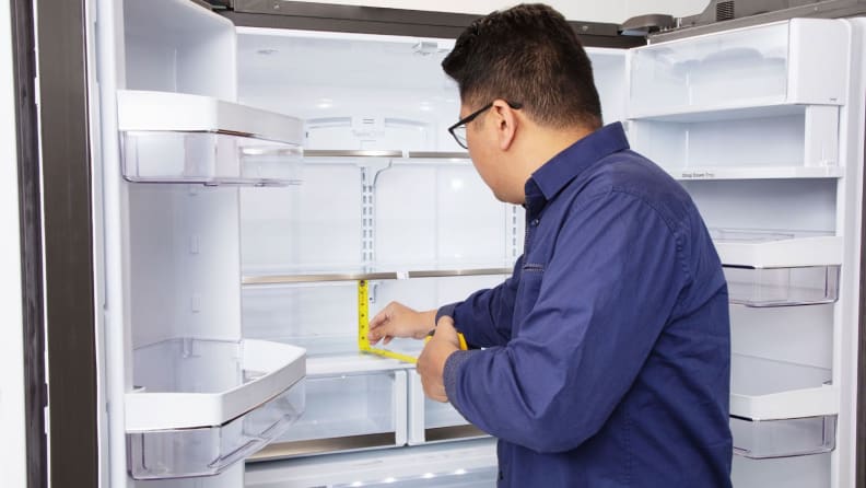Lab technician measures shelf height inside of refrigerator with measuring tape.