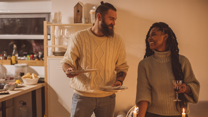 Two people laugh holding wine and plates of food