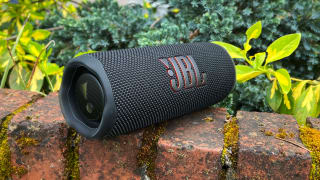 A black Bluetooth speaker with a JBL logo sits on a brick ledge.