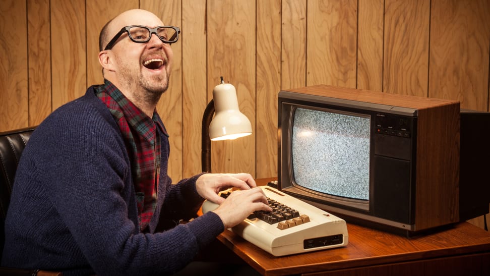 Person smiling while using fingers to type on retro keyboard in front of small television.