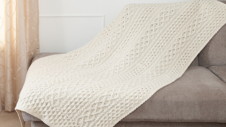 Cream colored Ireland's Eye knit throw blanket on grey couch