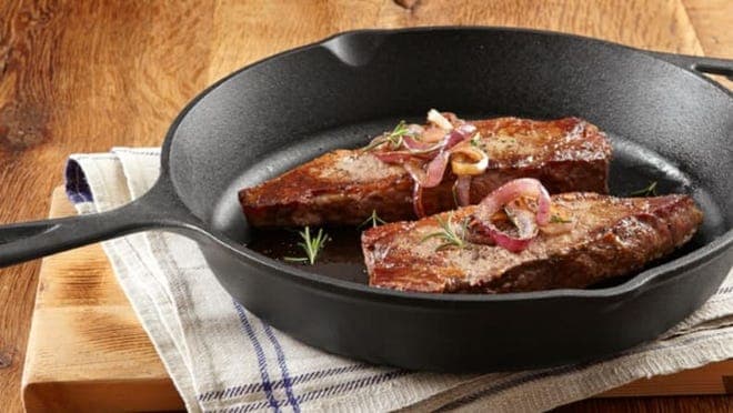 A cast iron skillet with seared meat on a kitchen table