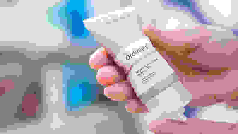 A person's hands squeezing moisturizer from a gray tube.