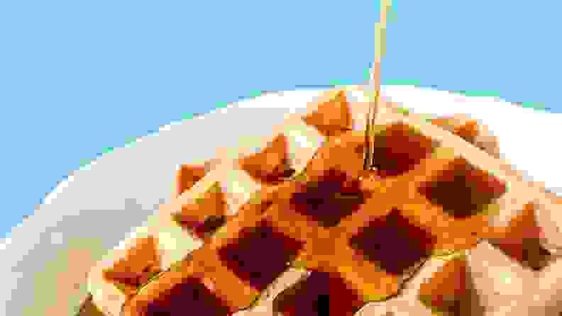 一个白色的盘子里装着两块方形华夫饼，上面浇上枫糖浆。