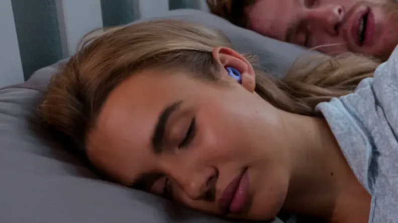 A woman sleeps on her side with blue CURVD earplugs in.