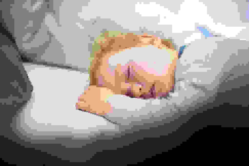 A blonde toddler sleeping in a bed with a pillow.