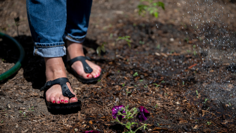一个女孩穿着Birkenstock Eva Gizeh凉鞋走过一个花园。