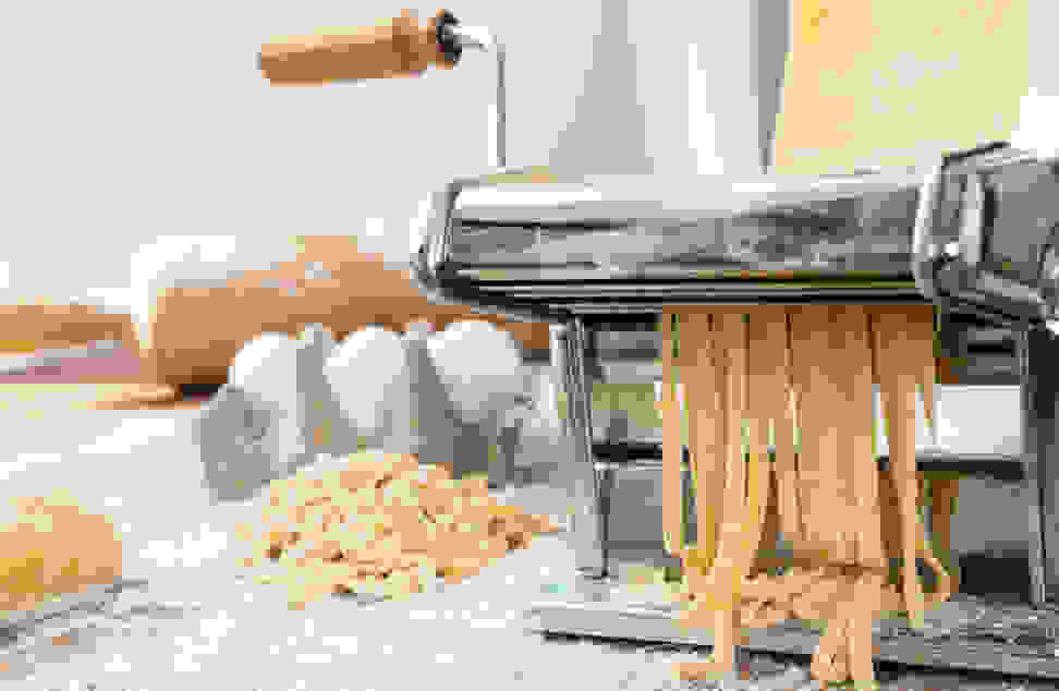 Eggs and freshly made noodles sit on a counter next to a hand-crank pasta maker.