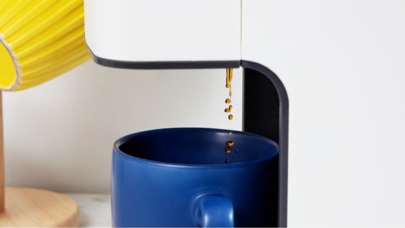 A blue mug with coffee dripping into it.