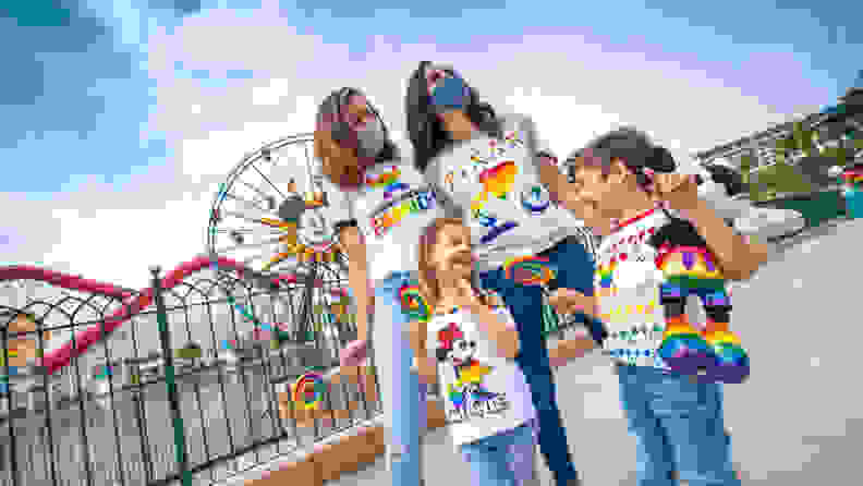 A family of four, all in Disney rainbow gear, at an amusement park, smiling.